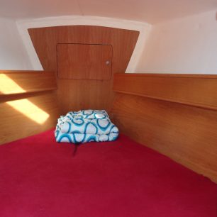 Pohled do majitelské příďové kajuty. Po bocích jsou poličky a dále se zde nachází jedna skříň s ramínky. Další úložný prostor je pod postelí.