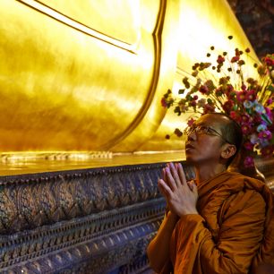 Modlící se mnich ve Wat Po u nohou ležícího Buddhy. Bangkok, Thajsko