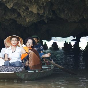 Čínští turisté na plavbě jeskyněmi v Tam Coc. Za nimi lodník pádlující pouze nohama, Vietnam