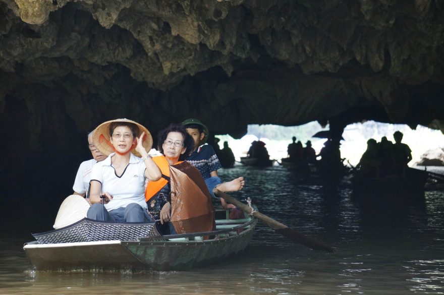 Čínští turisté na plavbě jeskyněmi v Tam Coc. Za nimi lodník pádlující pouze nohama, Vietnam