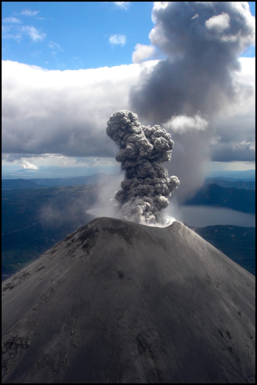 Vulkány dokonale kónických tvarů pokryté ledovci i sršící lávu a síru vyrůstají z nekonečné a bujné zelené tajgy, Kamčatka, Rusko